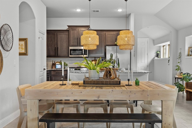 kitchen with decorative backsplash, dark brown cabinetry, pendant lighting, arched walkways, and stainless steel appliances