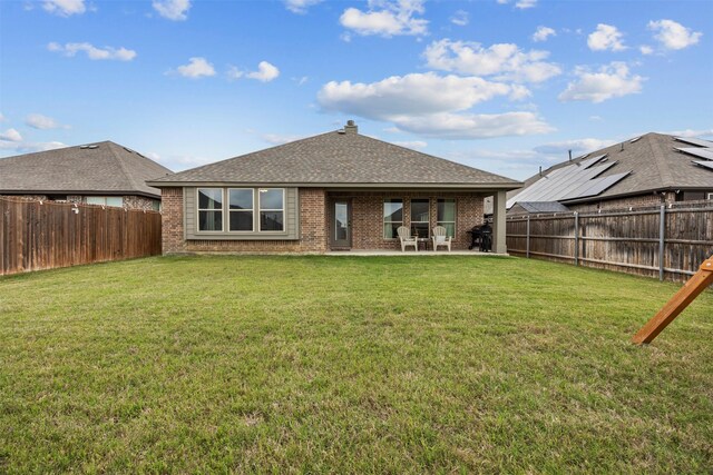 rear view of property with a fenced backyard, a patio, a lawn, and brick siding