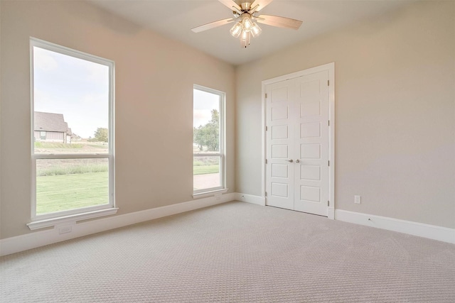 unfurnished room with a ceiling fan, baseboards, and light carpet