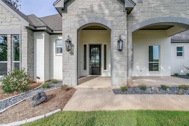 property entrance with brick siding, stone siding, and roof with shingles