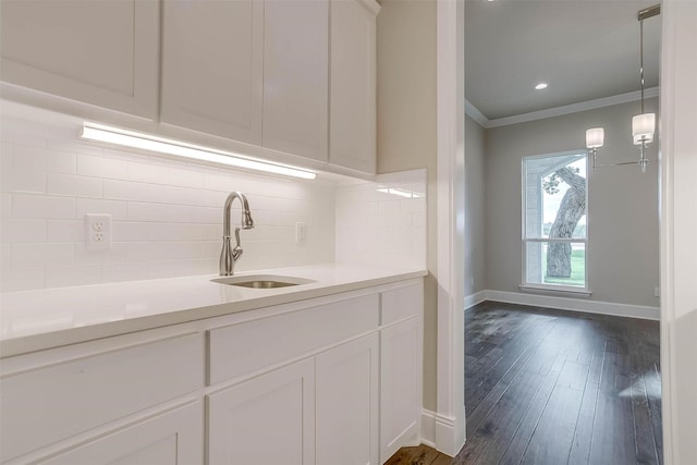 kitchen featuring white cabinets, a sink, light countertops, tasteful backsplash, and ornamental molding
