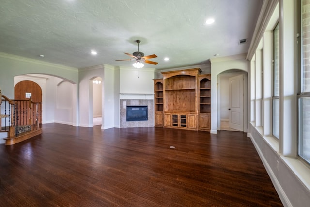 unfurnished living room featuring crown molding, ceiling fan, arched walkways, a glass covered fireplace, and visible vents