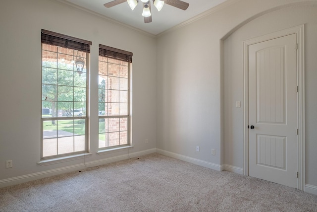 carpeted empty room with crown molding, a ceiling fan, and baseboards
