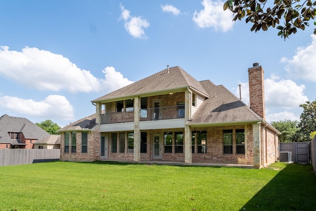 rear view of house with a balcony, a fenced backyard, a chimney, brick siding, and a lawn