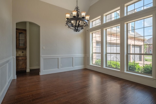 unfurnished dining area with dark wood-style flooring, arched walkways, an inviting chandelier, and a decorative wall
