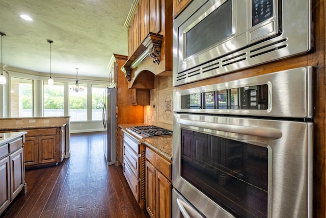 kitchen featuring light stone countertops, dark wood-style floors, brown cabinets, decorative light fixtures, and stainless steel appliances