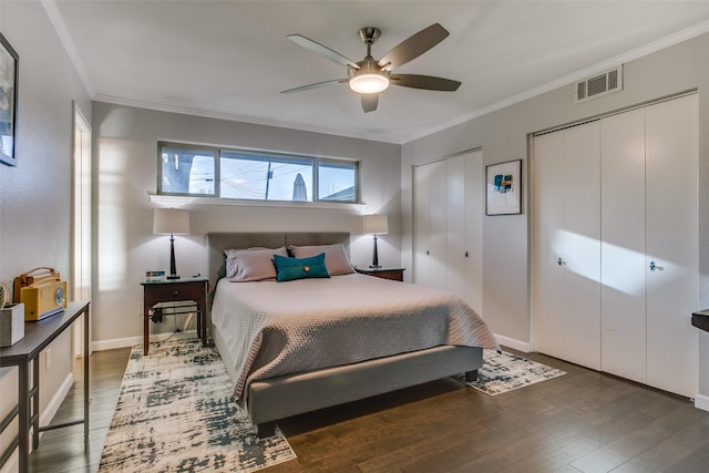 bedroom with crown molding, two closets, wood finished floors, and visible vents
