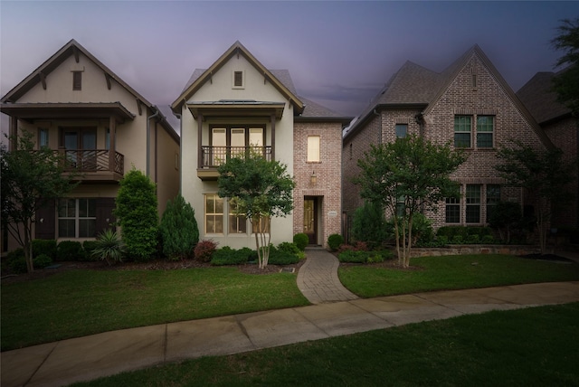 view of front of house featuring brick siding, a balcony, stucco siding, and a yard