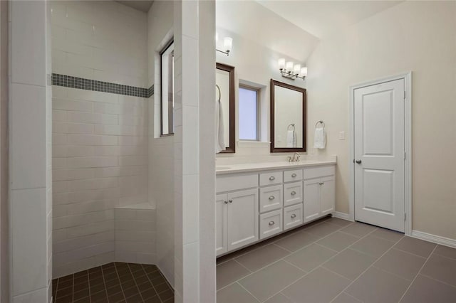 bathroom with a sink, tile patterned flooring, double vanity, baseboards, and tiled shower