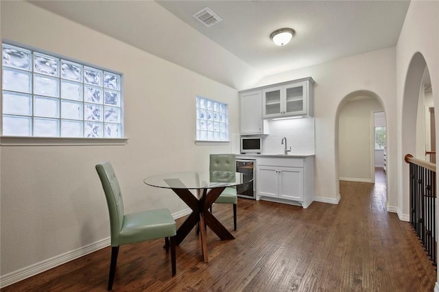 dining room featuring visible vents, arched walkways, dark wood finished floors, baseboards, and vaulted ceiling