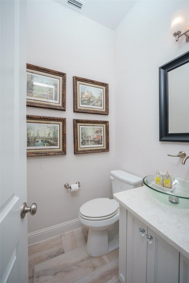 half bathroom with vanity, baseboards, toilet, and visible vents