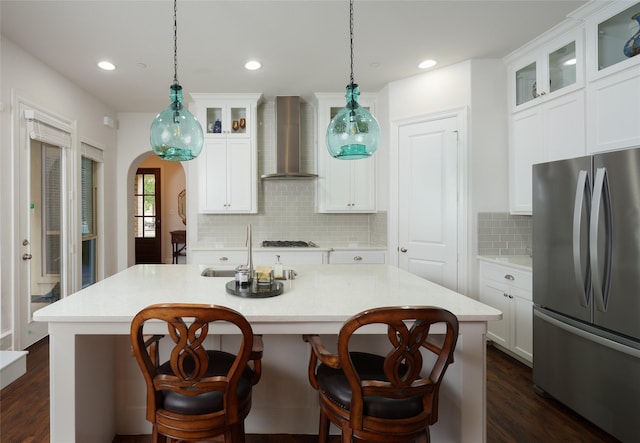 kitchen with freestanding refrigerator, dark wood-style floors, wall chimney range hood, arched walkways, and a sink