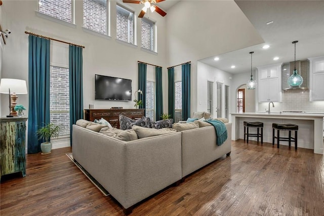 living area featuring a ceiling fan, dark wood finished floors, a towering ceiling, and arched walkways