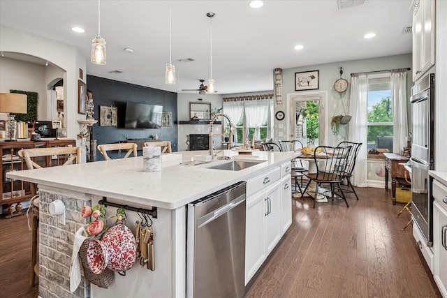 kitchen with a sink, dark wood finished floors, stainless steel appliances, white cabinetry, and pendant lighting