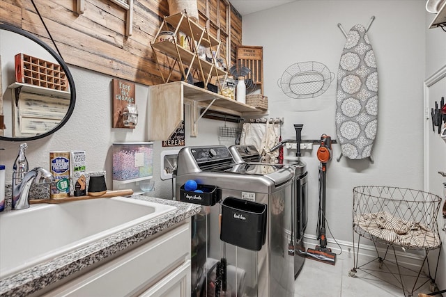 clothes washing area featuring laundry area, tile patterned flooring, washing machine and dryer, baseboards, and a sink