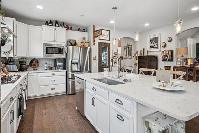 kitchen with dark wood-style flooring, a sink, arched walkways, stainless steel appliances, and a center island with sink