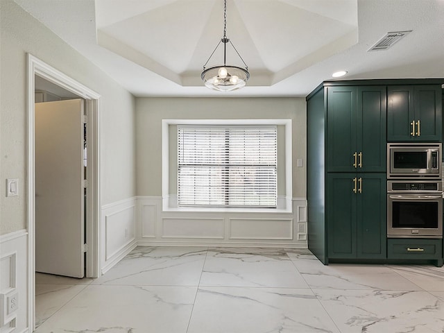 unfurnished dining area with visible vents, marble finish floor, a wainscoted wall, and a tray ceiling