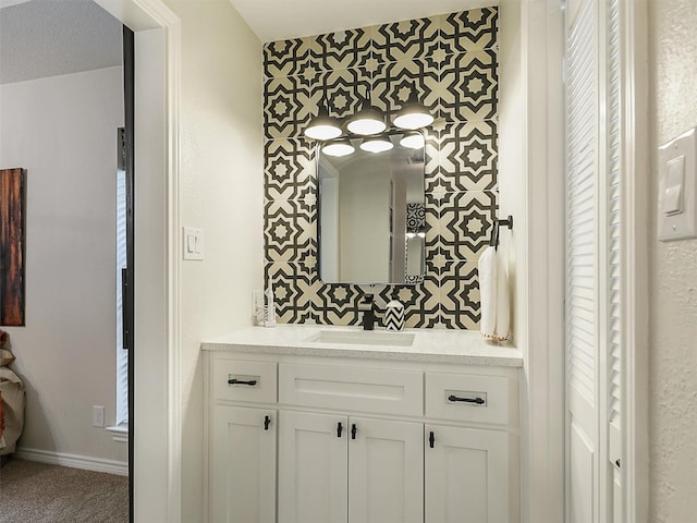 bathroom featuring vanity, baseboards, an accent wall, and wallpapered walls