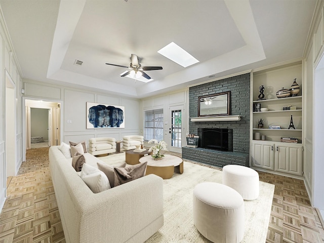 living area with ceiling fan, visible vents, a skylight, a fireplace, and a tray ceiling