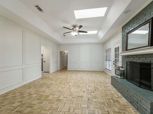 unfurnished living room with a fireplace, a decorative wall, a ceiling fan, a skylight, and visible vents