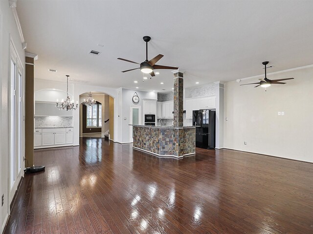 unfurnished living room with visible vents, dark wood-type flooring, ceiling fan with notable chandelier, and arched walkways