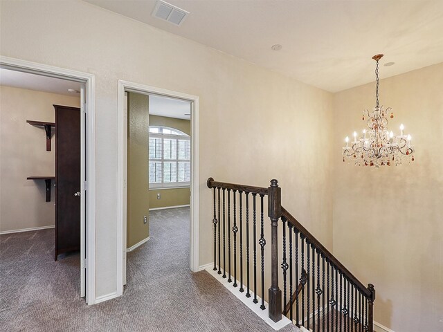 corridor with carpet floors, a chandelier, baseboards, an upstairs landing, and visible vents