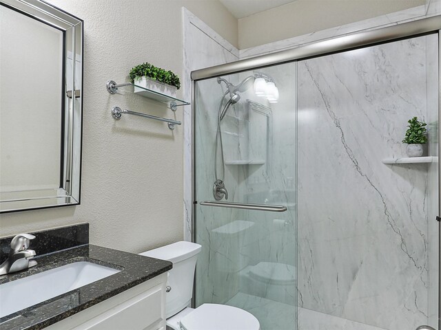 bathroom featuring toilet, a textured wall, a marble finish shower, and vanity