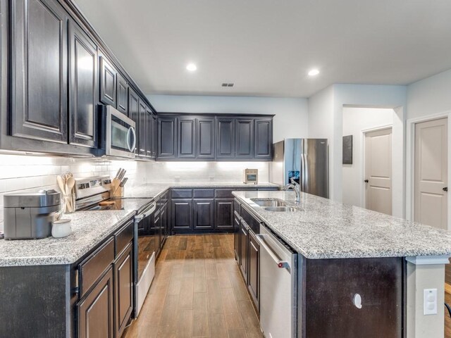 kitchen featuring a sink, stainless steel appliances, decorative backsplash, wood finished floors, and visible vents