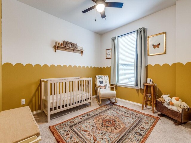 bedroom featuring a nursery area, baseboards, a ceiling fan, and carpet floors