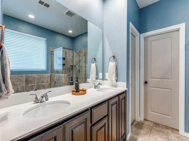 bathroom with visible vents, a sink, double vanity, and a shower stall