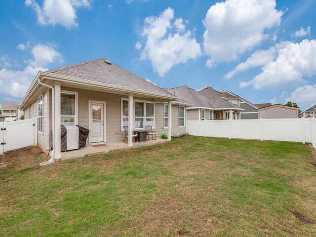 rear view of house featuring a lawn, a fenced backyard, a patio area, and a shingled roof