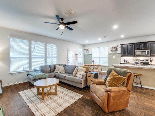 living room featuring ceiling fan, visible vents, baseboards, recessed lighting, and dark wood-type flooring