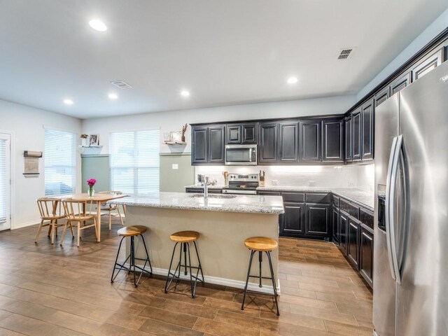 kitchen featuring dark wood-style flooring, visible vents, appliances with stainless steel finishes, a center island with sink, and a breakfast bar