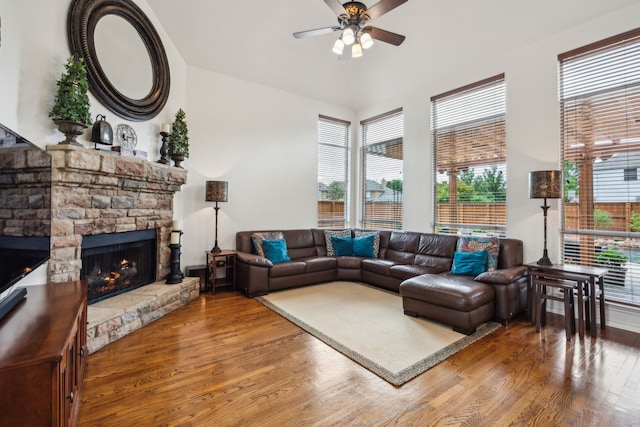 living area with ceiling fan, a stone fireplace, and wood finished floors