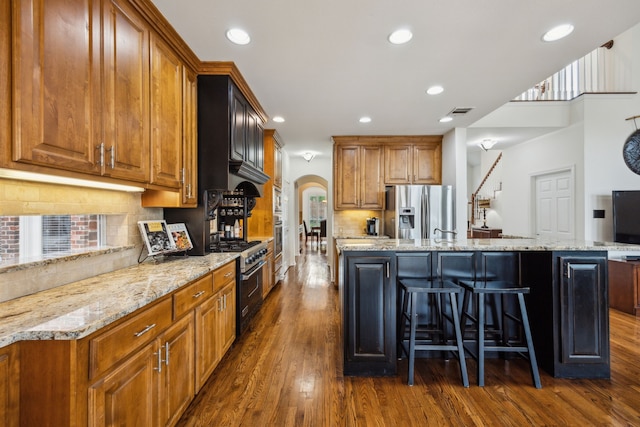 kitchen with a kitchen breakfast bar, backsplash, arched walkways, dark wood-style floors, and stainless steel appliances