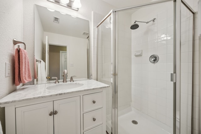 full bathroom featuring a textured wall, visible vents, a shower stall, and vanity
