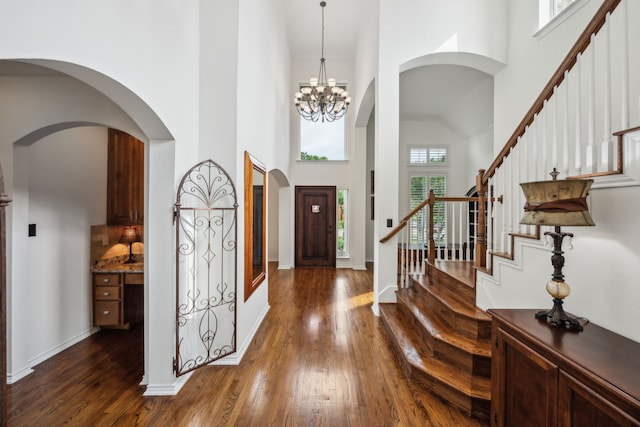 entryway with stairway, arched walkways, a high ceiling, and dark wood-style floors