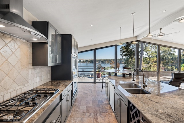 kitchen featuring stone tile flooring, light stone countertops, wall chimney exhaust hood, a sink, and appliances with stainless steel finishes