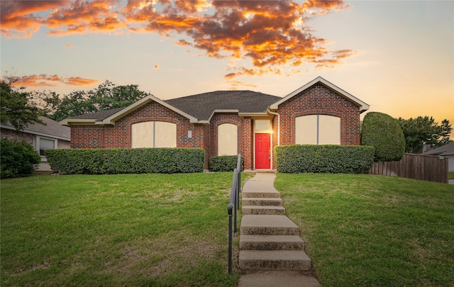 ranch-style house featuring roof with shingles, a yard, and brick siding