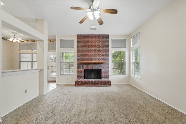 unfurnished living room featuring a brick fireplace, a ceiling fan, a wealth of natural light, and carpet