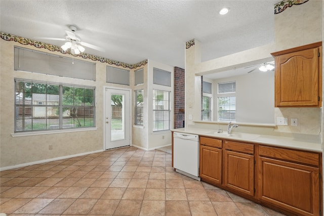 kitchen featuring a ceiling fan, baseboards, white dishwasher, light countertops, and a sink
