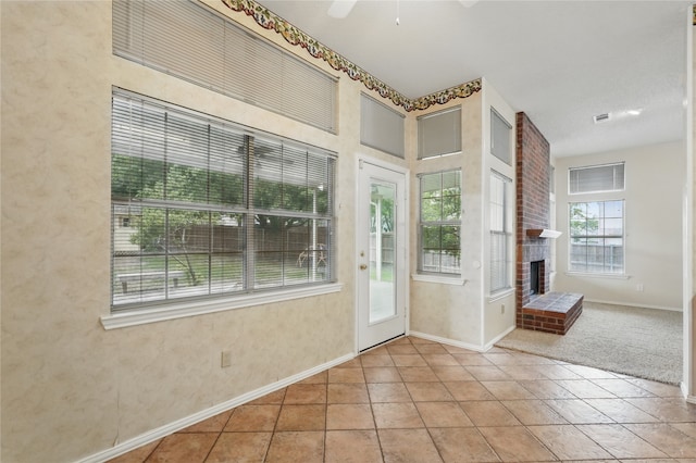 doorway to outside featuring visible vents, a brick fireplace, baseboards, ceiling fan, and tile patterned floors