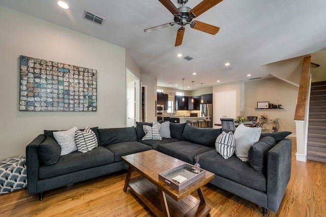 living area with light wood-style floors, ceiling fan, stairs, and visible vents