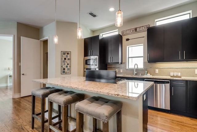 kitchen with a sink, dark cabinetry, stainless steel appliances, backsplash, and a kitchen island