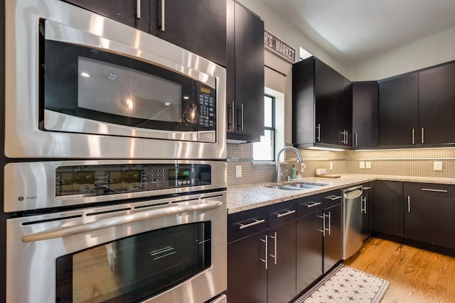 kitchen with light stone countertops, tasteful backsplash, a sink, light wood finished floors, and stainless steel appliances