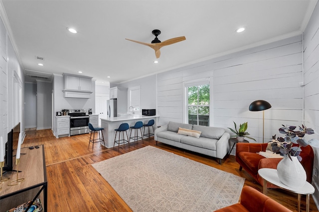 living area with a ceiling fan, visible vents, light wood finished floors, ornamental molding, and recessed lighting