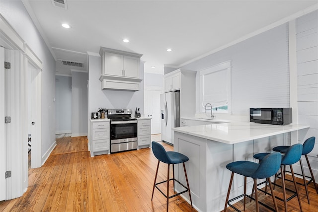 kitchen with visible vents, a peninsula, light wood-style floors, a kitchen breakfast bar, and appliances with stainless steel finishes