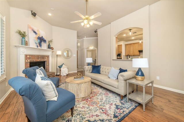 living room featuring arched walkways, a ceiling fan, baseboards, and light wood finished floors