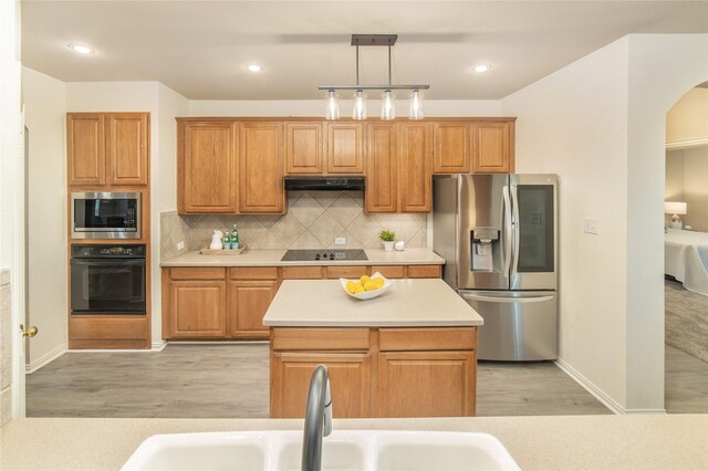 kitchen with a sink, light wood-style flooring, under cabinet range hood, and black appliances