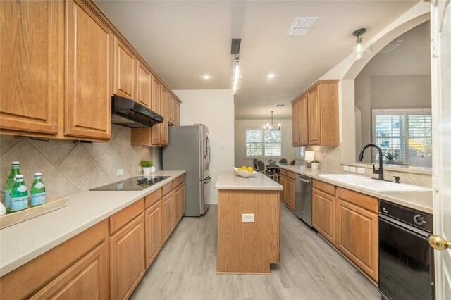 kitchen featuring visible vents, under cabinet range hood, a sink, light wood-style flooring, and stainless steel appliances